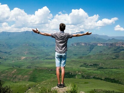 A man on a cliff with arms wide open absorbing his success