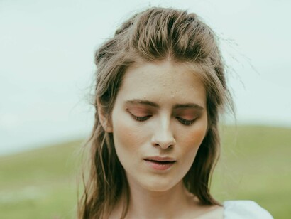 A young woman stands in a quiet, grassy landscape, her expression contemplative and introspective, symbolizing how the influx of information has profoundly altered our perception and interaction with the world, yet it often leaves us without a guiding framework to truly understand and navigate these changes