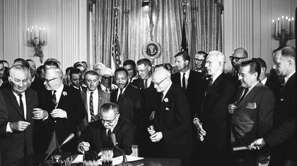 President Lyndon Johnson signs the Civil Rights Act of 1964; directly behind Johnson—Martin Luther King, Jr., Ralph Abernathy (directly behind King) and John Lewis (to the left of Abernathy)