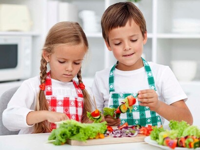 Dos niños preparando brochetas vegetales