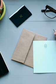 A person writing at a desk with a notebook and plant on