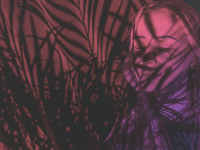 In the crimson illumination, under the sheltering veil of palm leaves, a woman stands in tranquil contemplation