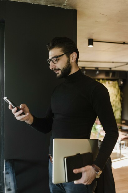 Man looking at his smartphone and holding a laptop