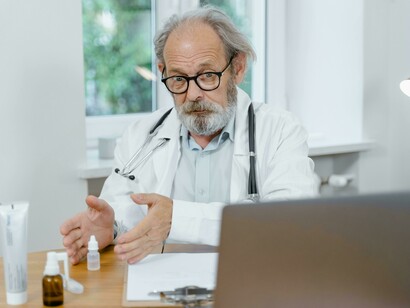 Un medico con barba, occhiali e stetoscopio al collo siede alla scrivania su cui ci sono prodotti farmaceutici: "Passavo le mie giornate camminando come zombi insieme agli altri ospiti lungo androni infiniti a smaltire le forti dosi di psicofarmaci che gli infermieri ci somministravano" 