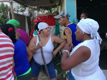 La gente baila y canta durante una ceremonia de santería. En el centro se puede ver un asistente de santero con redecilla blanca en el cabello. Mantilla, La Habana, Cuba