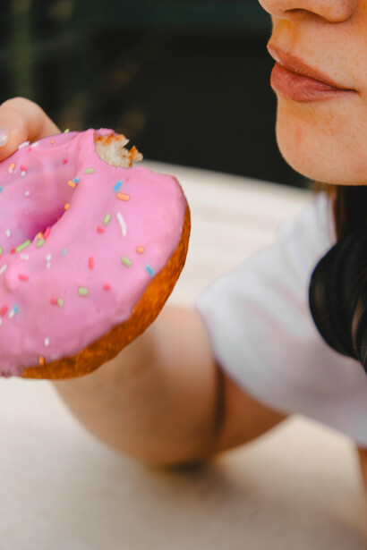 A close-up of a woman eating a donut, symbolizing the effects of sugar overload and the addictive pull of sugary, processed snacks