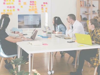 Employees at a startup with their individual laptops staring at a desktop screen to receive further information about the workspace tasks