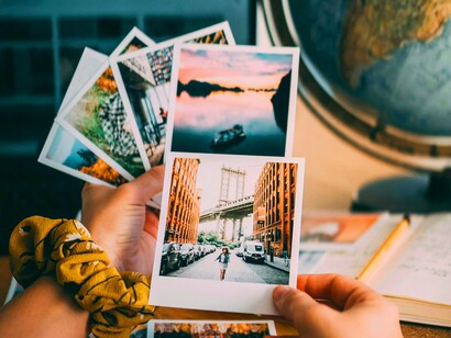 Jovem observa suas fotos. O migrante que encontra formas de expressar sua experiência de maneira criativa — seja por meio da arte, da literatura ou de outras formas de expressão — transforma sua saudade em algo que não apenas evoca o passado, mas também constrói o futuro