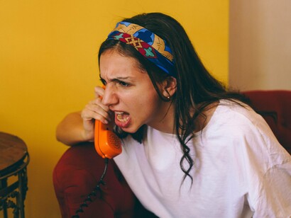 Sentada em um sofá vermelho, uma mulher grita ao telefone, tomada pela raiva. Para quem atende, uma explosão como essa pode ser apenas mais uma ligação; para quem a recebe, a violência das palavras pode deixar marcas que não são visíveis