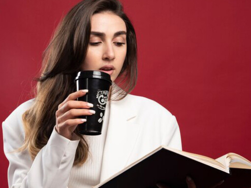 A female journalist holding a cup while reviewing notes in her notebook, fully engaged in her work
