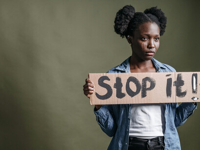 A woman in a blue denim jacket holds a cardboard sign, reflecting silent struggle and the sense of being misunderstood
