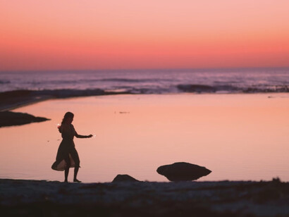 As the sun sets in a stunning display of pink and purple, she strolls along the beach, embracing the freedom of self-discovery and authenticity