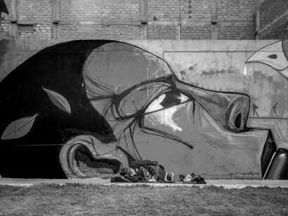 A homeless man rests on a sofa on the street, surrounded by colorful graffiti on the wall behind him
