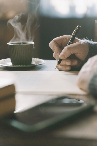 A person busy writing and having a cup of tea