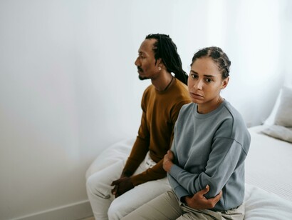 A couple sitting separately on a bed, reflecting tension and emotional distance