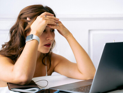 A woman multitasking with a smartphone, smartwatch, and laptop shows signs of exhaustion from digital media overload