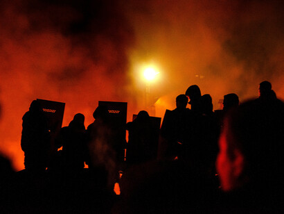 Silhouettes of people standing in a field at night, gathered quietly behind police barricades