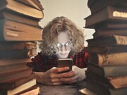 A young boy scrolling, glued to his smartphone while ignoring the piles of old books in front of him; an image that reflects the reality of the youth in our current generation, all about their smartphones and movie platforms, rejecting the good old novels