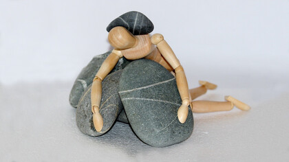 Overwhelmed by the weight of burnout, a struggle symbolized by a toy human beneath crushing stones