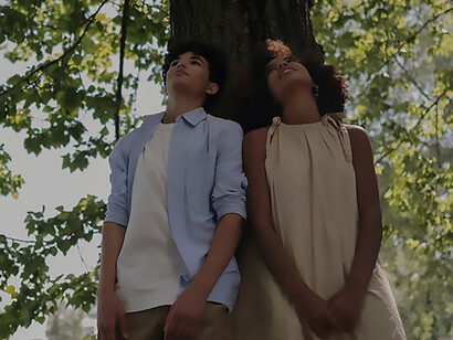 In the park, a young boy and girl on their first date stroll hand in hand, sharing smiles, finding a serene spot to sit, and savoring the sweet anticipation of a burgeoning connection