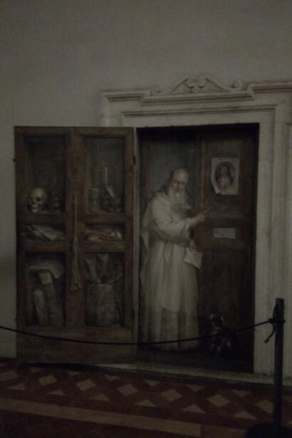 Porta a trompe-l’oeil di Filippo Balbi (1885), da cui sembra affacciarsi il Certosino Fercoldo, raffigurato con gli oggetti della vita quotidiana dei monaci della Certosa