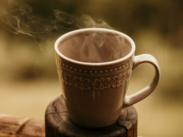 Uma caneca de café fumegante repousa sobre um pequeno suporte de madeira. O café aparece no relato como parte da rotina das antigas oficinas, acompanhando o trabalho e os momentos de pausa entre uma tarefa e outra