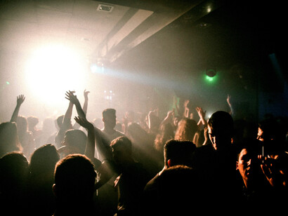A celebrating crowd fills the dance floor, illuminated by club lighting and driven by dance music