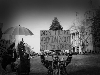 A man in front of the lawn of the US Supreme Court is holding a sign that says "don't like abortion? cut your dick off" 