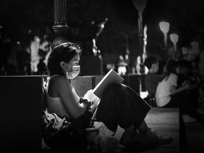 Jovem lê sentada na rua, escapando para outros mundos e alheia ao mau-estar produzido pela pandemia