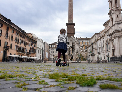 Roma, 18 abril 2020: en una Plaza Navona desierta con el pasto que ha logrado crecer entre los ladrillos del pavimento una niñita corre en su monopatín (Esma Cakir/Agencia DHA)