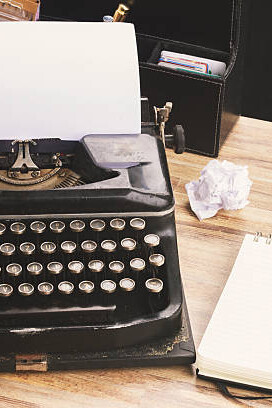A vintage typewriter sits atop a wooden desk, accompanied by historical diaries and literary archives