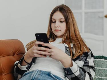 A girl lies on a couch, absorbed in endless scrolling on her smartphone