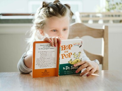 A young girl reading her first book on the kitchen table which she found at the library