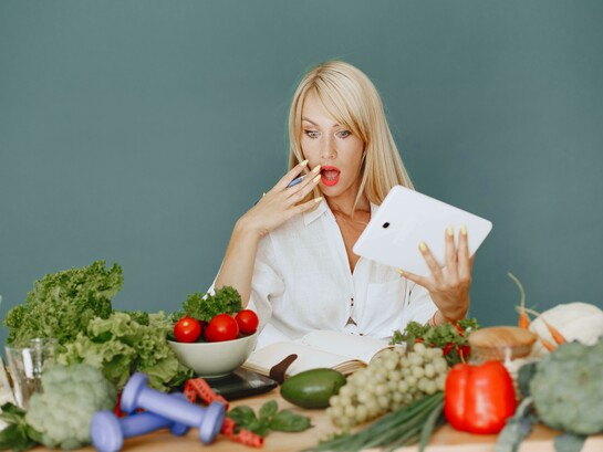 Woman holding a tablet and making a surprised face while looking at a table full of vegetables