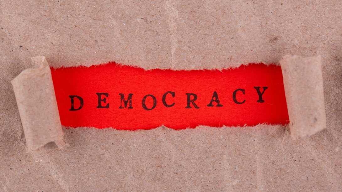 Illustrazione con etichetta "democrazia" scritta in rosso:" Abbiamo già assistito a una perdita dei valori democratici, dei capisaldi costituzionali, del modo di pensare collettivo che partiva dal presupposto di alcune regole di base condivise, fulcro del nostro modo di vivere, che hanno caratterizzato tutto il dopoguerra fino a qualche anno fa"