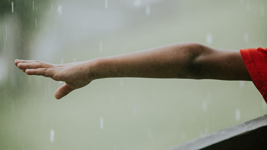 Menino de uniforme vermelho sente a chuva cair em sua mão