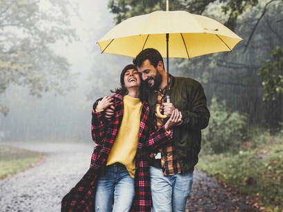A romantic couple strolls closely together under an umbrella in a fog-covered autumn woodland