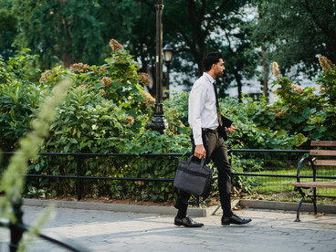 A man in a suit sitting on a brown wooden bench, looking for a job
