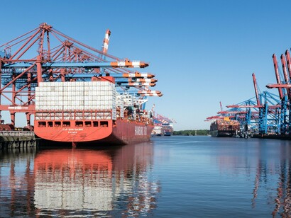 A massive container ship docked at a busy port, representing the global trade networks at the heart of economic power