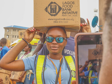 Women carrying cardboard boxes on their heads stand in a food aid distribution line, reflecting the impact of the hunger crisis in Lagos, Nigeria