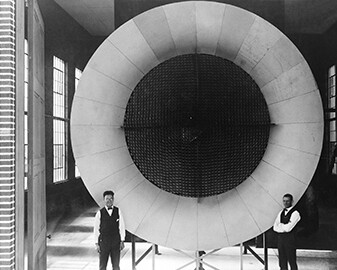 Langley's First Wind Tunnel, ca. 1920
The honeycombed, screened center of this open-circuit air intake for Langley's first wind tunnel ensured a steady, non-turbulent flow of air. Two mechanics pose near the entrance end of the actual tunnel, where air was pulled into the test section through a honeycomb arrangement to smoothen the flow. 
Courtesy NASA Langley Research Center