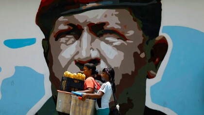 Dos adolescentes venezolanas pasan por delante de un mural de Hugo Chávez en Caracas