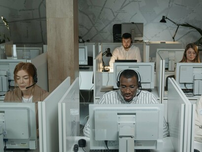 Profissionais trabalham diante dos computadores em um ambiente de atendimento ao cliente. Por trás de cada voz que responde a uma ligação existe uma pessoa que também carrega histórias, necessidades e desafios