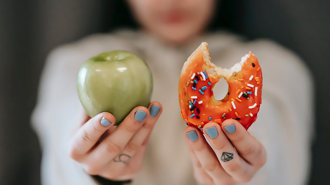 Woman holding an apple in one hand and a donut in the other emphasizes the importance of a preventive diet against cancer