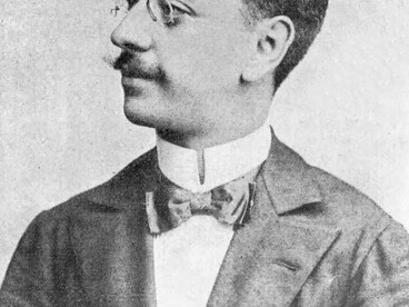 Olavo Bilac em um retrato de perfil, usando terno, gravata e óculos, em uma fotografia em preto e branco. A imagem remete ao poeta parnasiano cuja obra exemplifica a atenção ao rigor formal e ao uso cuidadoso das palavras, mostrando como a escolha e a organização da linguagem também podem funcionar como recursos de construção de sentido e persuasão