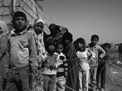 A black-and-white photograph captures war-affected children and adults, their faces marked by hunger and sorrow