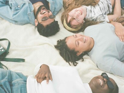 A group of people of all races and genders lying down on a towel looking up to the sky and smiling or laughing for no apparent reason