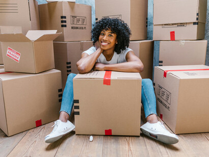 A happy woman sitting on the floor surrounded by moving boxes