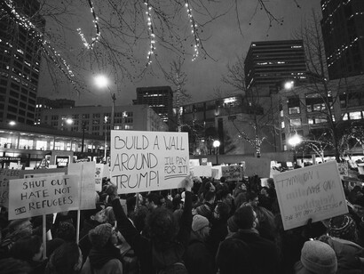 With signs raised in solidarity, demonstrators confront the scapegoating of immigrants used to obscure deeper crises of emoluments abuse and executive overreach