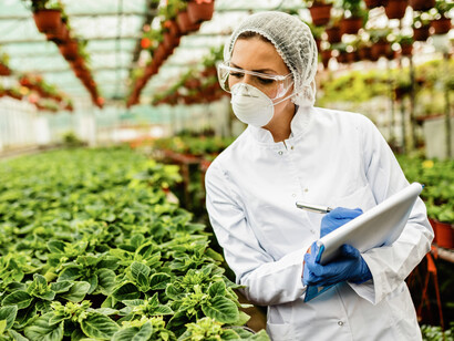 A female scientist inspects the growth of potted flowers and takes notes in a greenhouse, illustrating the spirit of biotechnology innovation and futuristic agriculture